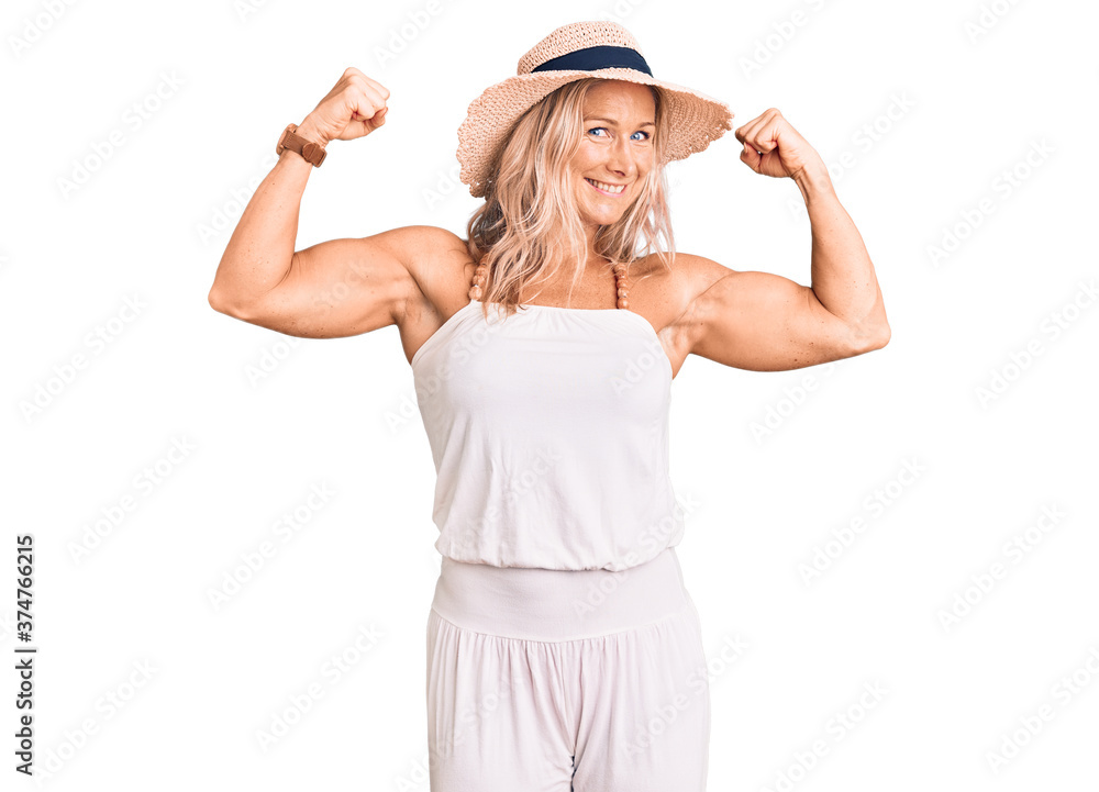 Middle age fit blonde woman wearing summer hat showing arms muscles smiling proud. fitness concept. Middle age fit blonde woman wearing summer hat showing arms muscles smiling proud. fitness concept.