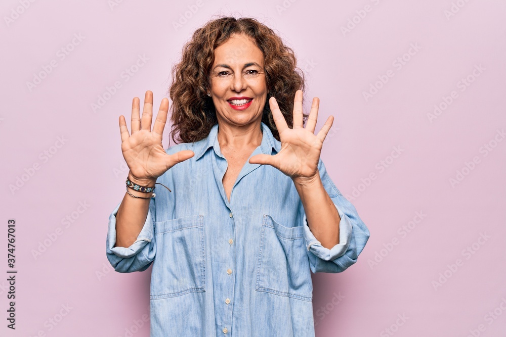 Middle age beautiful woman wearing casual denim shirt standing over pink background showing and pointing up with fingers number ten while smiling confident and happy. Middle age beautiful woman wearing casual denim shirt standing over pink background showing and pointing up with fingers number ten while smiling confident and happy.