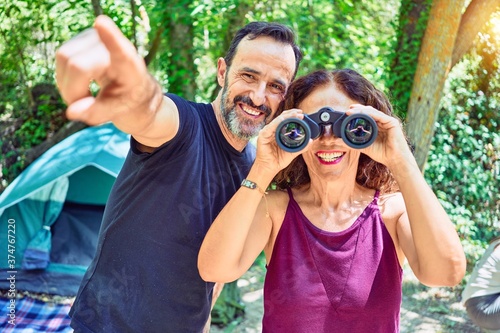 Middle age couple  of hiker camping at the forest. Smiiling happy using binoculars pointing to the side with finger. photo