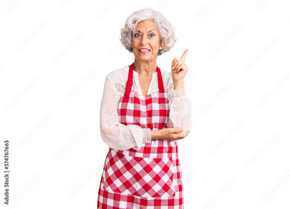 Senior grey-haired woman wearing apron smiling happy pointing with hand and finger to the side Senior grey-haired woman wearing apron smiling happy pointing with hand and finger to the side