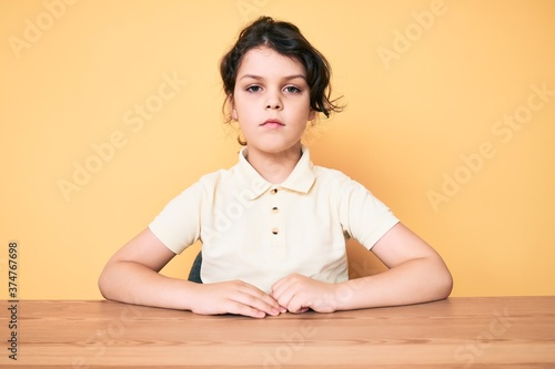 Cute hispanic child wearing casual clothes sitting on the table with serious expression on face. simple and natural looking at the camera.