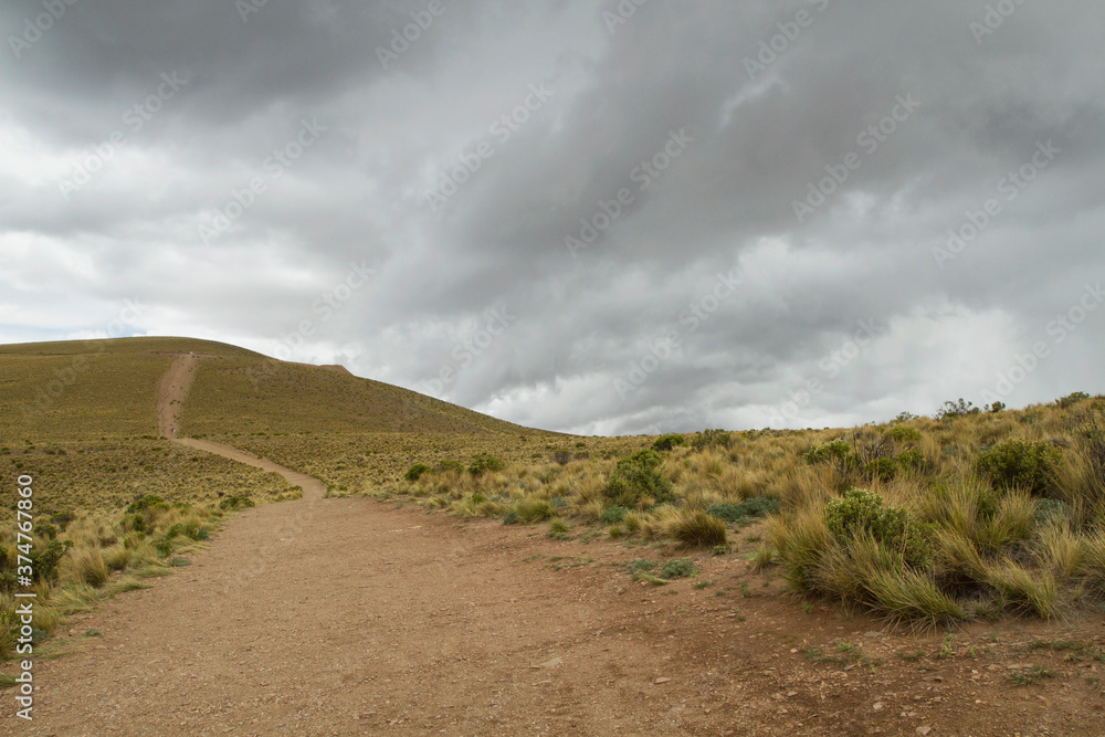 The dirt path along the hill and yellow grassland under a cloudy sky. The dirt path along the hill and yellow grassland under a cloudy sky.