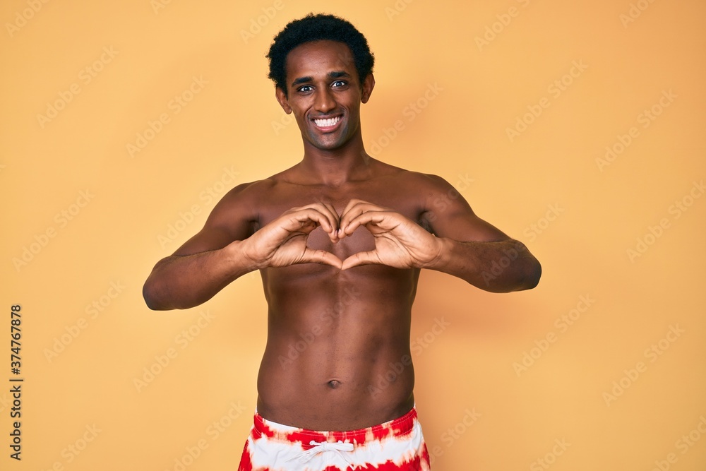 African handsome man wearing swimsuit smiling in love showing heart symbol and shape with hands. romantic concept.