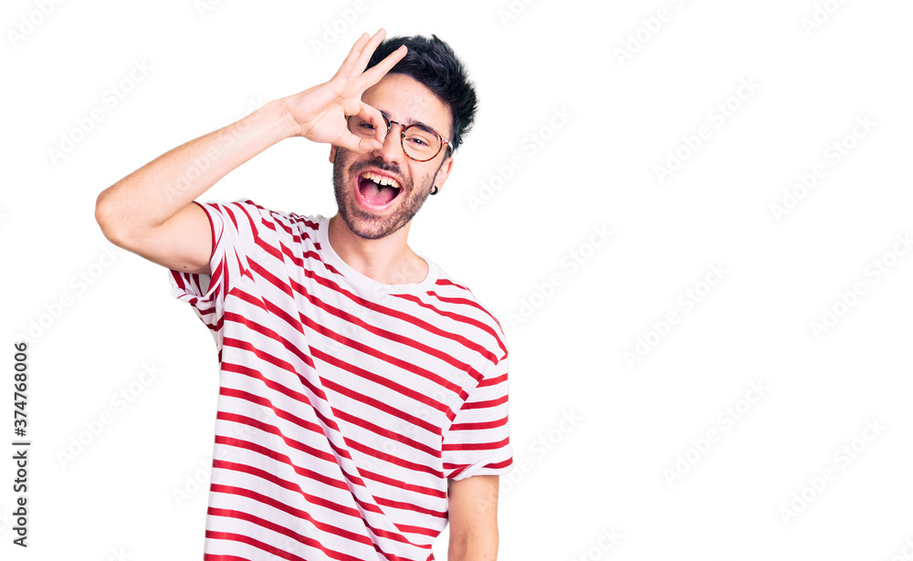 Young hispanic man wearing casual clothes doing ok gesture with hand smiling, eye looking through fingers with happy face. Young hispanic man wearing casual clothes doing ok gesture with hand smiling, eye looking through fingers with happy face.
