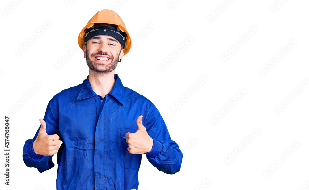 Young hispanic man wearing worker uniform success sign doing positive gesture with hand, thumbs up smiling and happy. cheerful expression and winner gesture.