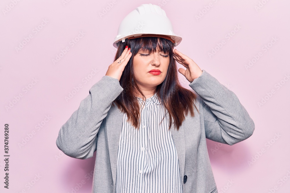 Young plus size woman wearing architect hardhat with hand on head, headache because stress. suffering migraine. Young plus size woman wearing architect hardhat with hand on head, headache because stress. suffering migraine.