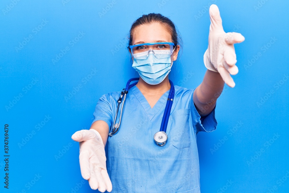 Young blonde woman wearing doctor uniform and coronavirus protection holding help reminder looking at the camera smiling with open arms for hug. cheerful expression embracing happiness. Young blonde woman wearing doctor uniform and coronavirus protection holding help reminder looking at the camera smiling with open arms for hug. cheerful expression embracing happiness.