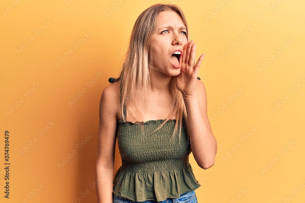 Young blonde woman wearing casual clothes shouting and screaming loud to side with hand on mouth. communication concept. Young blonde woman wearing casual clothes shouting and screaming loud to side with hand on mouth. communication concept.