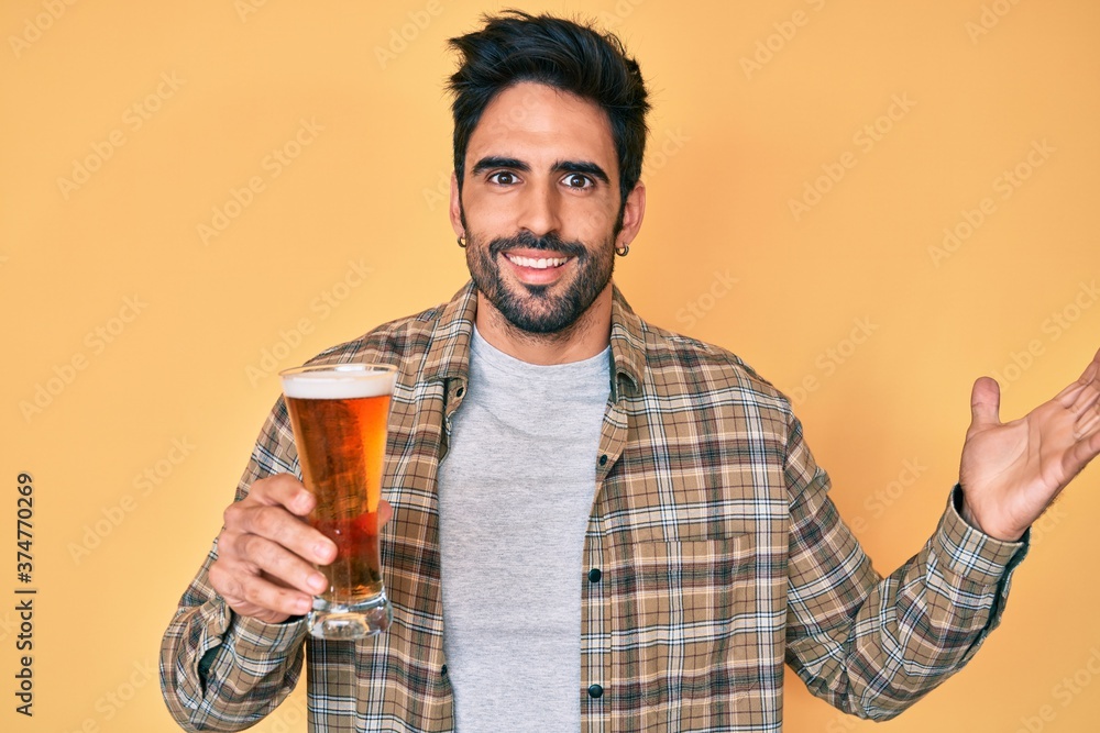 Handsome hispanic man with beard drinking a pint of beer celebrating victory with happy smile and winner expression with raised hands Handsome hispanic man with beard drinking a pint of beer celebrating victory with happy smile and winner expression with raised hands