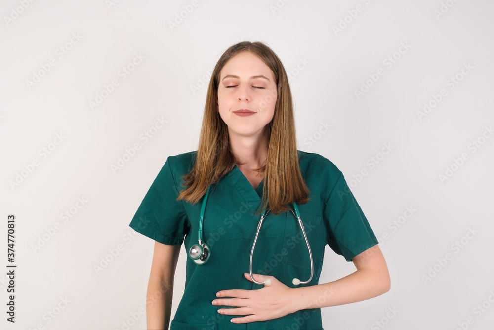Female doctor wearing a green scrubs and stethoscope touches tummy, smiles gently, eating and satisfaction concept. Female doctor wearing a green scrubs and stethoscope touches tummy, smiles gently, eating and satisfaction concept.