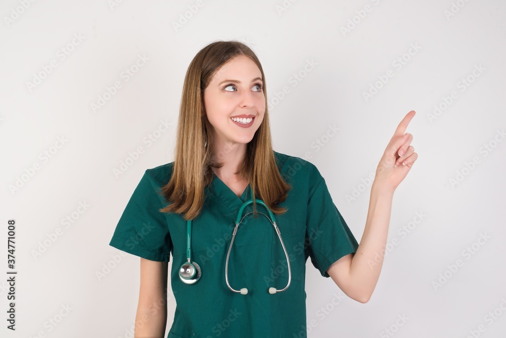 Smiling Female doctor wearing a green scrubs and stethoscope pointing up and looking at the camera Smiling Female doctor wearing a green scrubs and stethoscope pointing up and looking at the camera