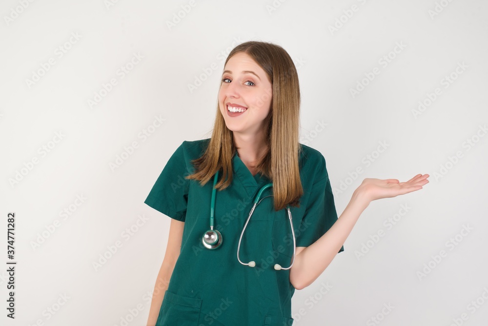 Female doctor wearing a green scrubs and stethoscope smiling cheerful presenting and pointing with palm of hand looking at the camera. Female doctor wearing a green scrubs and stethoscope smiling cheerful presenting and pointing with palm of hand looking at the camera.