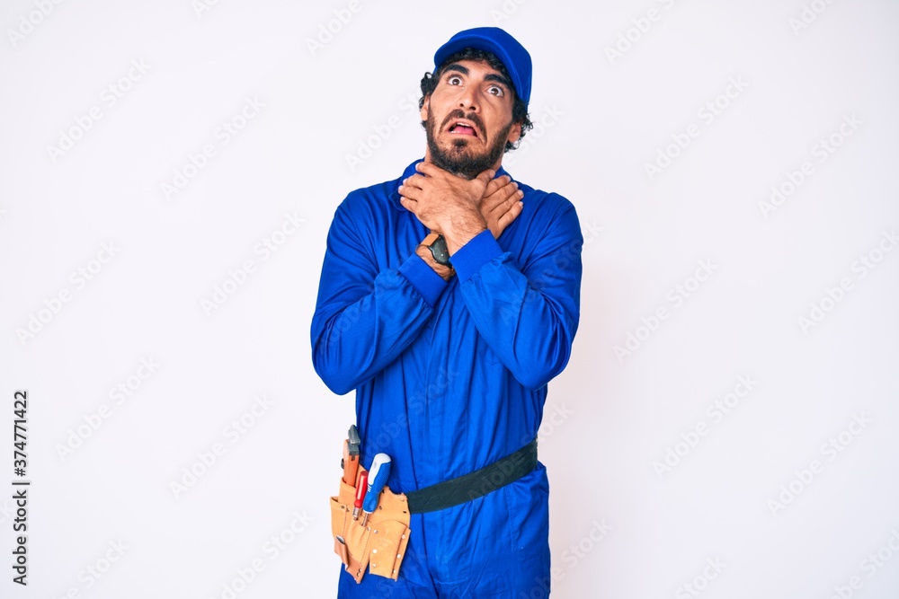 Handsome young man with curly hair and bear weaing handyman uniform shouting suffocate because painful strangle. health problem. asphyxiate and suicide concept. Handsome young man with curly hair and bear weaing handyman uniform shouting suffocate because painful strangle. health problem. asphyxiate and suicide concept.