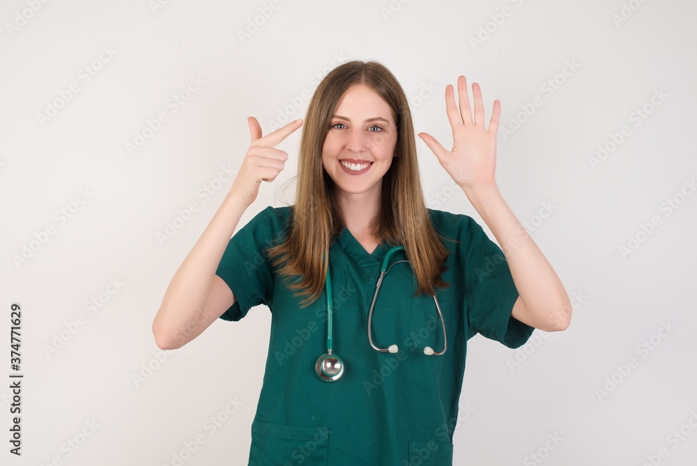 Female doctor wearing a green scrubs and stethoscope showing and pointing up with fingers number seven while smiling confident and happy. Female doctor wearing a green scrubs and stethoscope showing and pointing up with fingers number seven while smiling confident and happy.