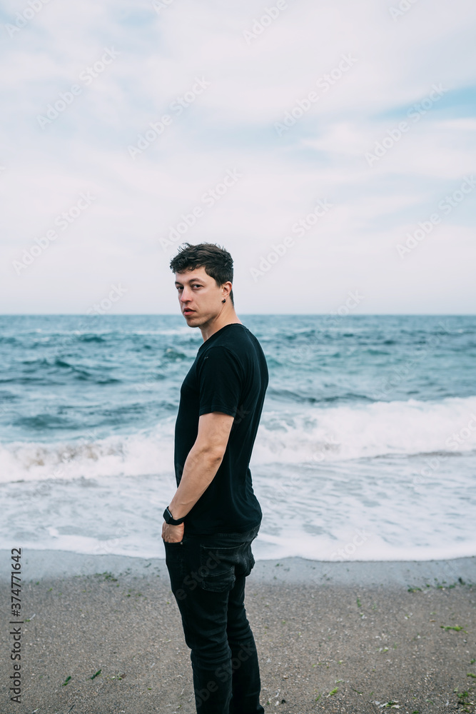 Smiling guy in a black T-shirt stands on the sandy seashore. Smiling guy in a black T-shirt stands on the sandy seashore.