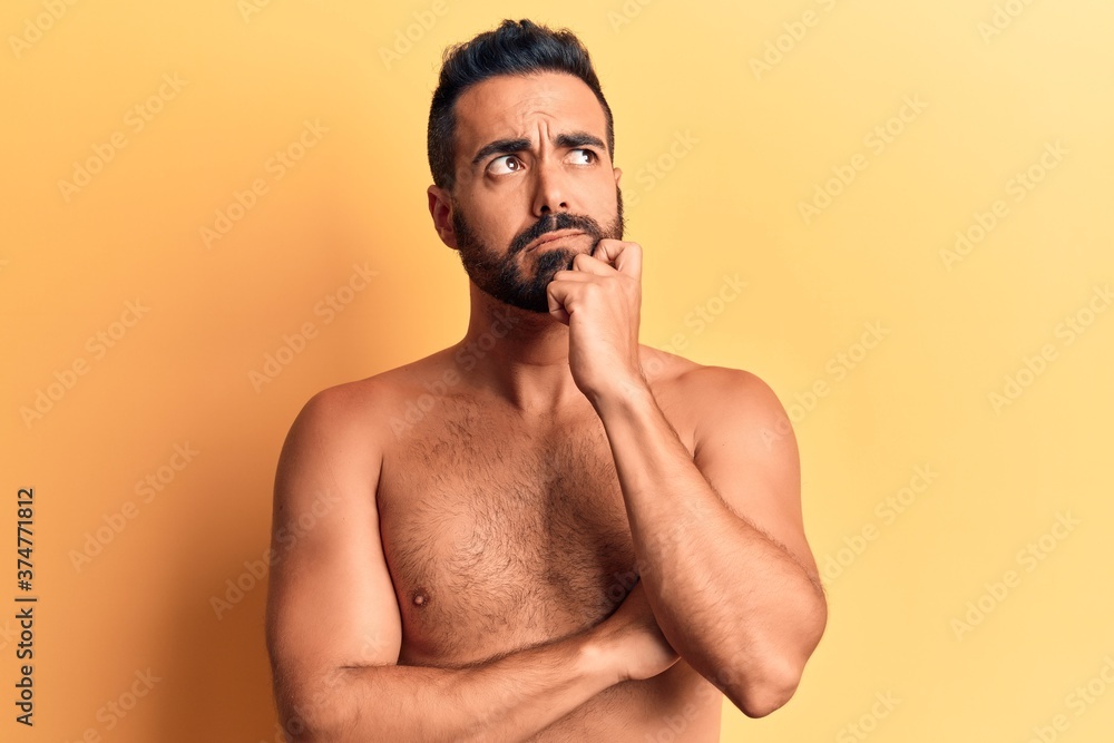 Fototapeta premium Young hispanic man standing shirtless serious face thinking about question with hand on chin, thoughtful about confusing idea