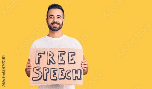 Young hispanic man holding free speech banner looking positive and happy standing and smiling with a confident smile showing teeth