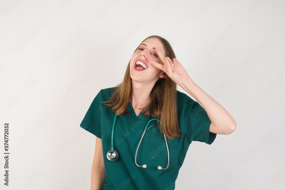 Female doctor wearing a green scrubs and stethoscope Doing peace symbol with fingers over face, smiling cheerful showing victory Female doctor wearing a green scrubs and stethoscope Doing peace symbol with fingers over face, smiling cheerful showing victory