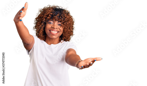 Young african american woman wearing casual white tshirt looking at the camera smiling with open arms for hug. cheerful expression embracing happiness.