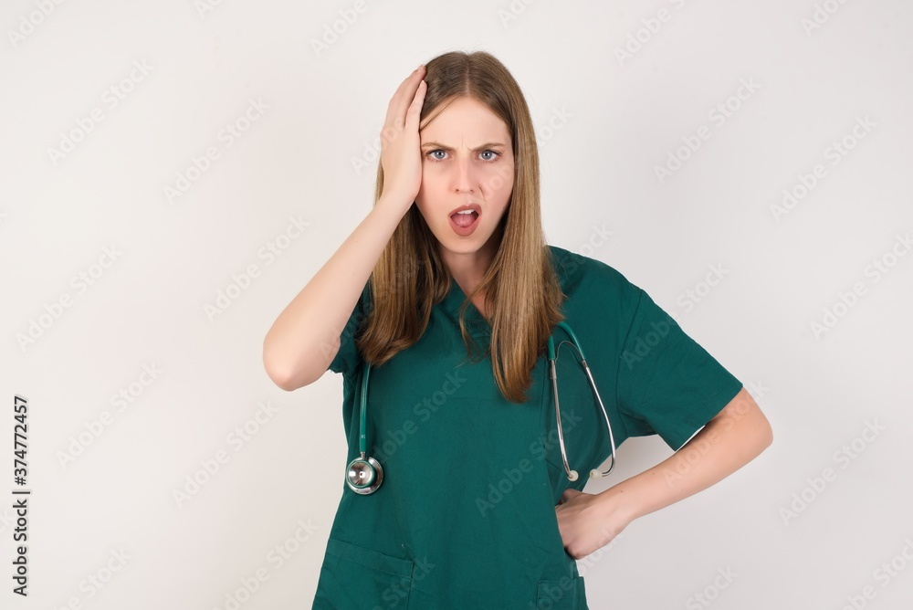 Embarrassed attractive Female doctor wearing a green scrubs and stethoscope, with shocked expression, expresses great amazement, Puzzled man poses indoor Embarrassed attractive Female doctor wearing a green scrubs and stethoscope, with shocked expression, expresses great amazement, Puzzled man poses indoor