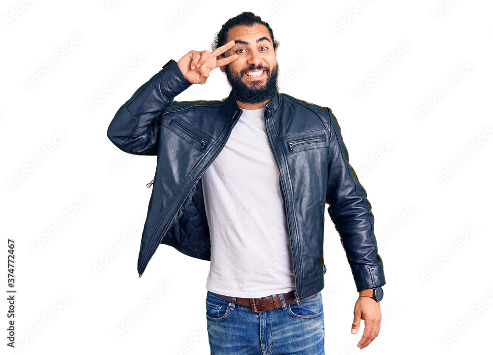 Fototapeta premium Young arab man wearing casual leather jacket doing peace symbol with fingers over face, smiling cheerful showing victory