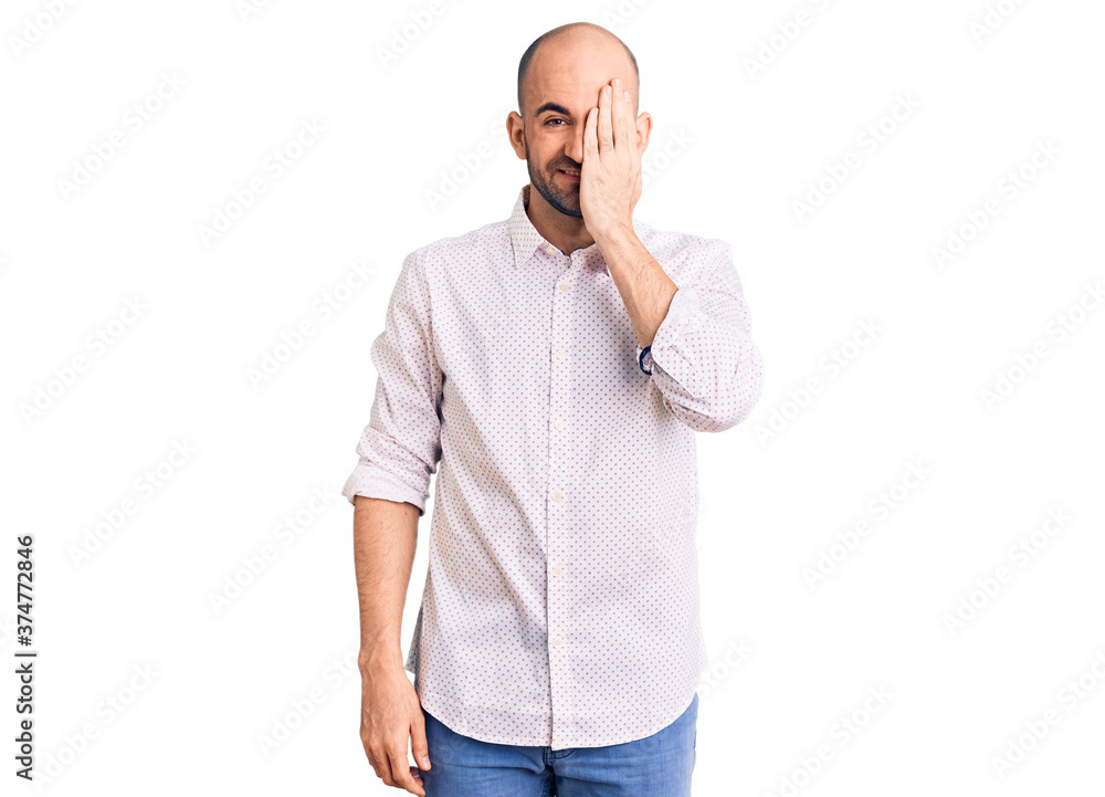 Young handsome man wearing elegant shirt covering one eye with hand, confident smile on face and surprise emotion. Young handsome man wearing elegant shirt covering one eye with hand, confident smile on face and surprise emotion.