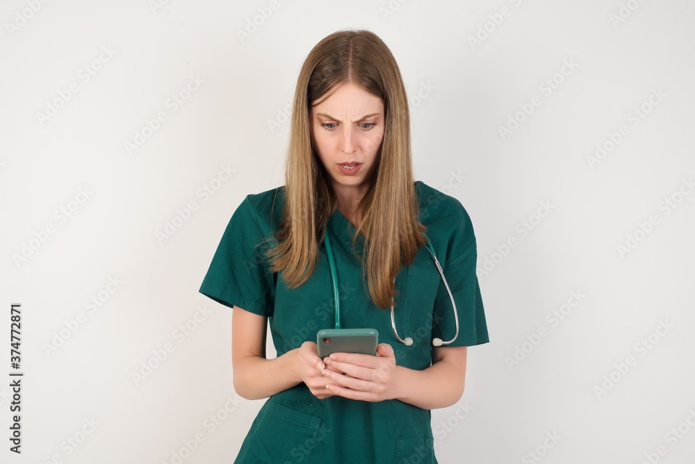 Portrait of focused Female doctor wearing a green scrubs and stethoscopeuse smartphone reading social media news, or important e-mail Portrait of focused Female doctor wearing a green scrubs and stethoscopeuse smartphone reading social media news, or important e-mail