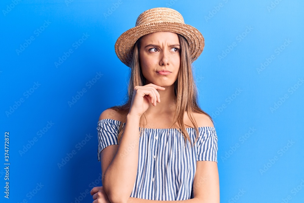 Young beautiful girl wearing summer hat and striped t-shirt thinking concentrated about doubt with finger on chin and looking up wondering Young beautiful girl wearing summer hat and striped t-shirt thinking concentrated about doubt with finger on chin and looking up wondering