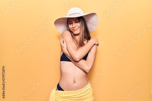 Young beautiful girl wearing bikini and hat hugging oneself happy and positive  smiling confident. self love and self care