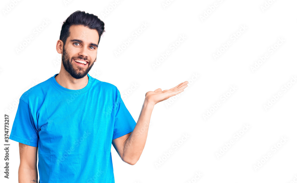 Young handsome man with beard wearing casual t-shirt smiling cheerful presenting and pointing with palm of hand looking at the camera. Young handsome man with beard wearing casual t-shirt smiling cheerful presenting and pointing with palm of hand looking at the camera.
