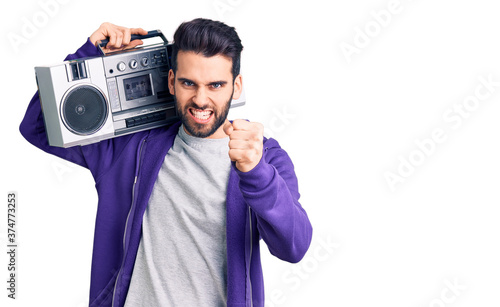 Young handsome man with beard listening to music using vintage boombox annoyed and frustrated shouting with anger, yelling crazy with anger and hand raised