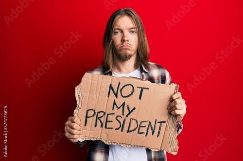 Handsome caucasian man with long hair holding not my president protest banner depressed and worry for distress, crying angry and afraid. sad expression.