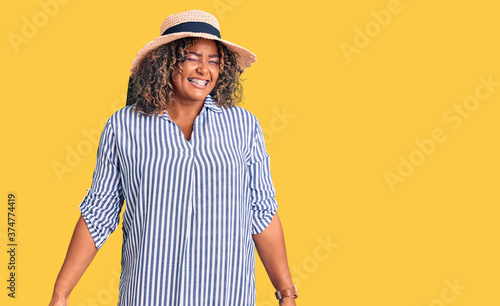 Young african american plus size woman wearing summer hat winking looking at the camera with sexy expression, cheerful and happy face.
