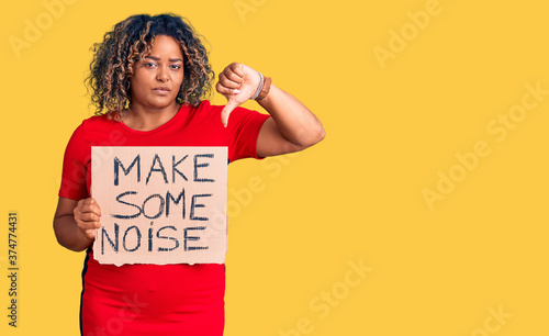 Young african american plus size woman holding make some noise banner with angry face, negative sign showing dislike with thumbs down, rejection concept photo