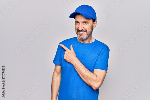 Middle age handsome deliveryman wearing cap standing over isolated white background smiling cheerful pointing with hand and finger up to the side