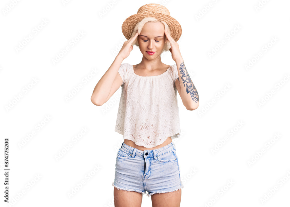Young blonde woman with tattoo wearing summer hat with hand on head for pain in head because stress. suffering migraine. Young blonde woman with tattoo wearing summer hat with hand on head for pain in head because stress. suffering migraine.