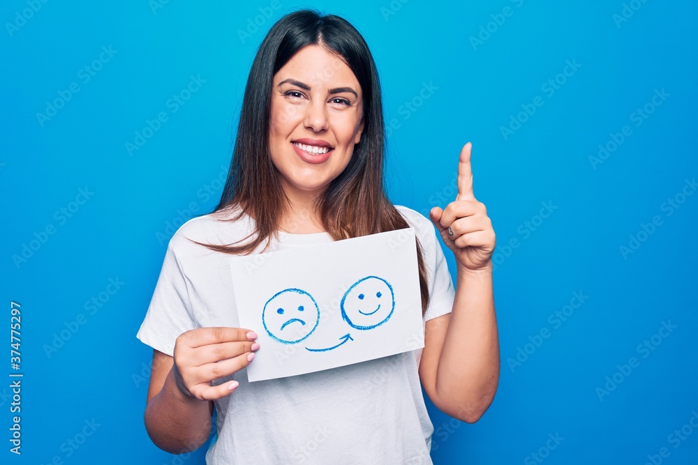 Woman asking for psychology change holding paper with unhappy to happy emotion message smiling with an idea or question pointing finger with happy face, number one Woman asking for psychology change holding paper with unhappy to happy emotion message smiling with an idea or question pointing finger with happy face, number one