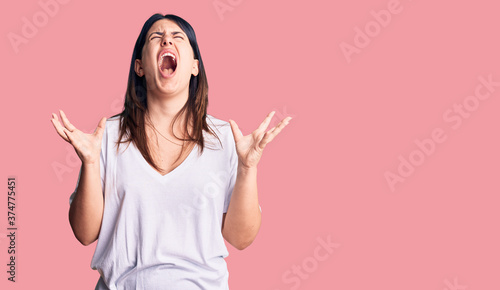 Young beautiful brunette woman wearing casual t-shirt crazy and mad shouting and yelling with aggressive expression and arms raised. frustration concept.