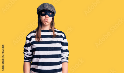 Young beautiful brunette woman wearing burglar mask puffing cheeks with funny face. mouth inflated with air, crazy expression.