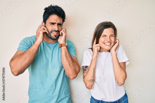 Beautiful young couple of boyfriend and girlfriend together covering ears with fingers with annoyed expression for the noise of loud music. deaf concept.