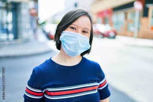 Beautiful brunette woman with down syndrome at the town on a sunny day wearing safety medical mask for coronavirus