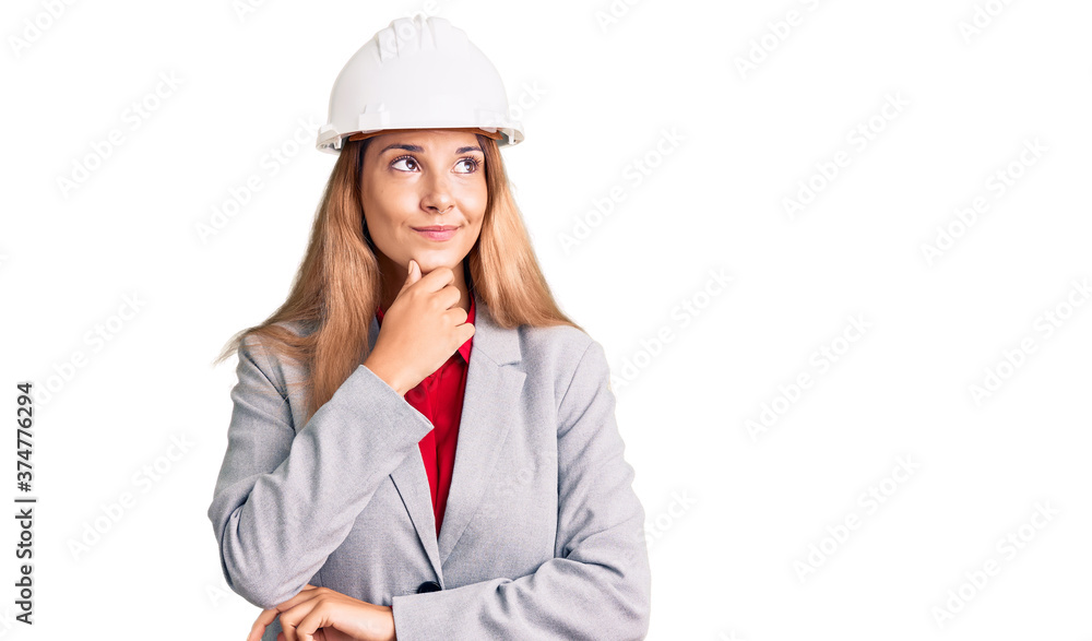 Beautiful young woman wearing architect hardhat with hand on chin thinking about question, pensive expression. smiling with thoughtful face. doubt concept.