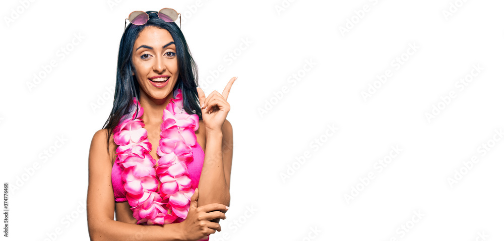 Beautiful hispanic woman wearing bikini and hawaiian lei with a big smile on face, pointing with hand and finger to the side looking at the camera. Beautiful hispanic woman wearing bikini and hawaiian lei with a big smile on face, pointing with hand and finger to the side looking at the camera.