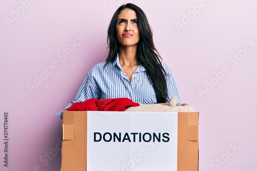 Beautiful hispanic woman volunteer holding donations box angry and mad screaming frustrated and furious, shouting with anger looking up. © Krakenimages.com