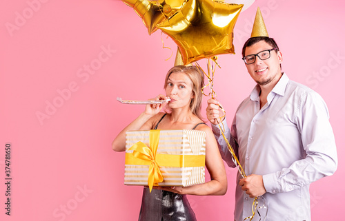 Happy laughing couple celebrating birthday party holding golden balloons and gift box isolated on pink backgrownd photo