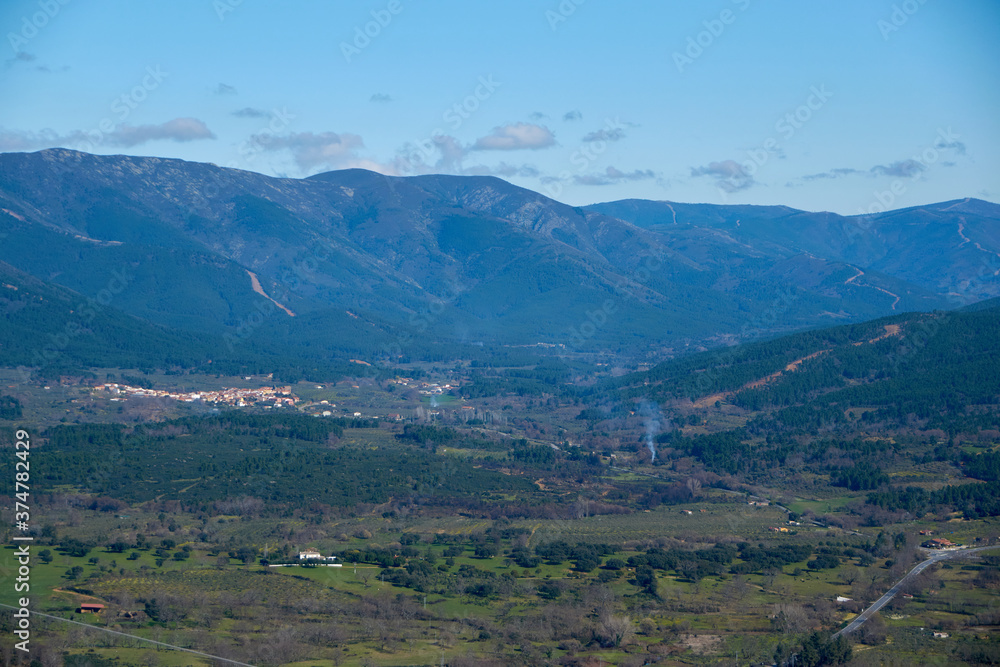 panoramic view of a mountain valley landscape with some clouds and a small village