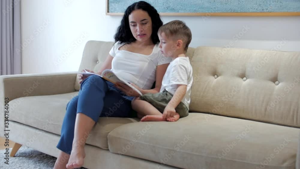 Happy family, mom and cute preschool boy, son and mom read a book together, sitting on the sofa at home, mom reads fiction, enjoy family moments. Happy family, mom and cute preschool boy, son and mom read a book together, sitting on the sofa at home, mom reads fiction, enjoy family moments.