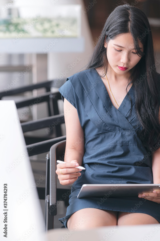 Portrait of young asian woman using tablet computer white sitting on the chair in co-workspace. Portrait of young asian woman using tablet computer white sitting on the chair in co-workspace.