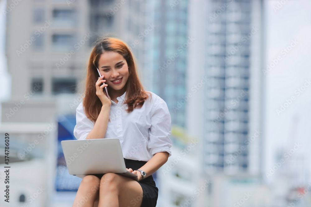 Fototapeta premium Smiling confident young Asian business woman using laptop for job at outside office.