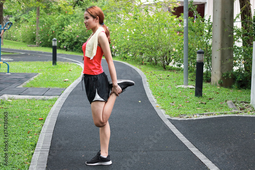 Healthy Asian woman stretching her legs before run in park. Fitness and exercise concept.
